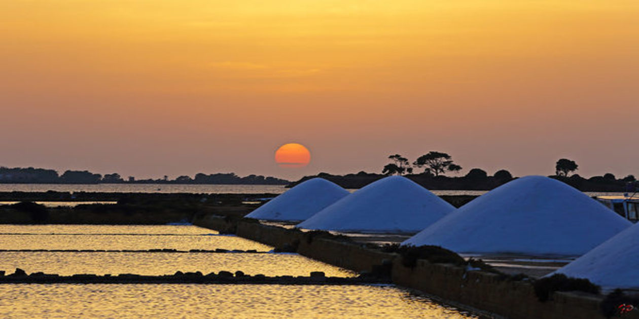 L'immagine mostra il tramonto del sole sulla sulla Riserva Naturale Saline di Trapani e Paceco