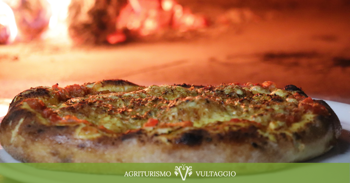 In primo piano la nostra pizza cotta a forno a legna sullo sfondo della bocca del forno con il fuoco che arde.
